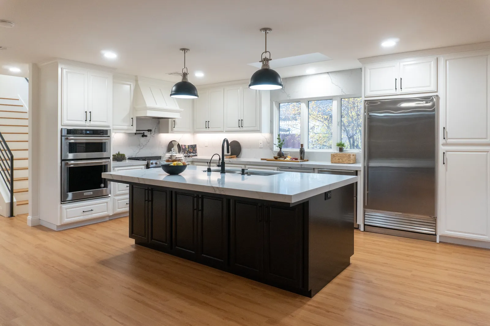 Bright white kitchen with a black island, marble-look counters, and stainless built-in refrigerator by KHB Construction