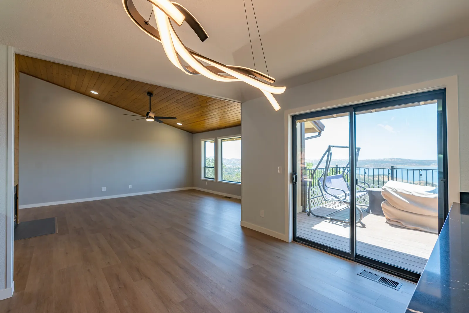 Open living room with a wood-plank vaulted ceiling, sculptural pendant light, and sliding glass doors to a deck overlooking a lake