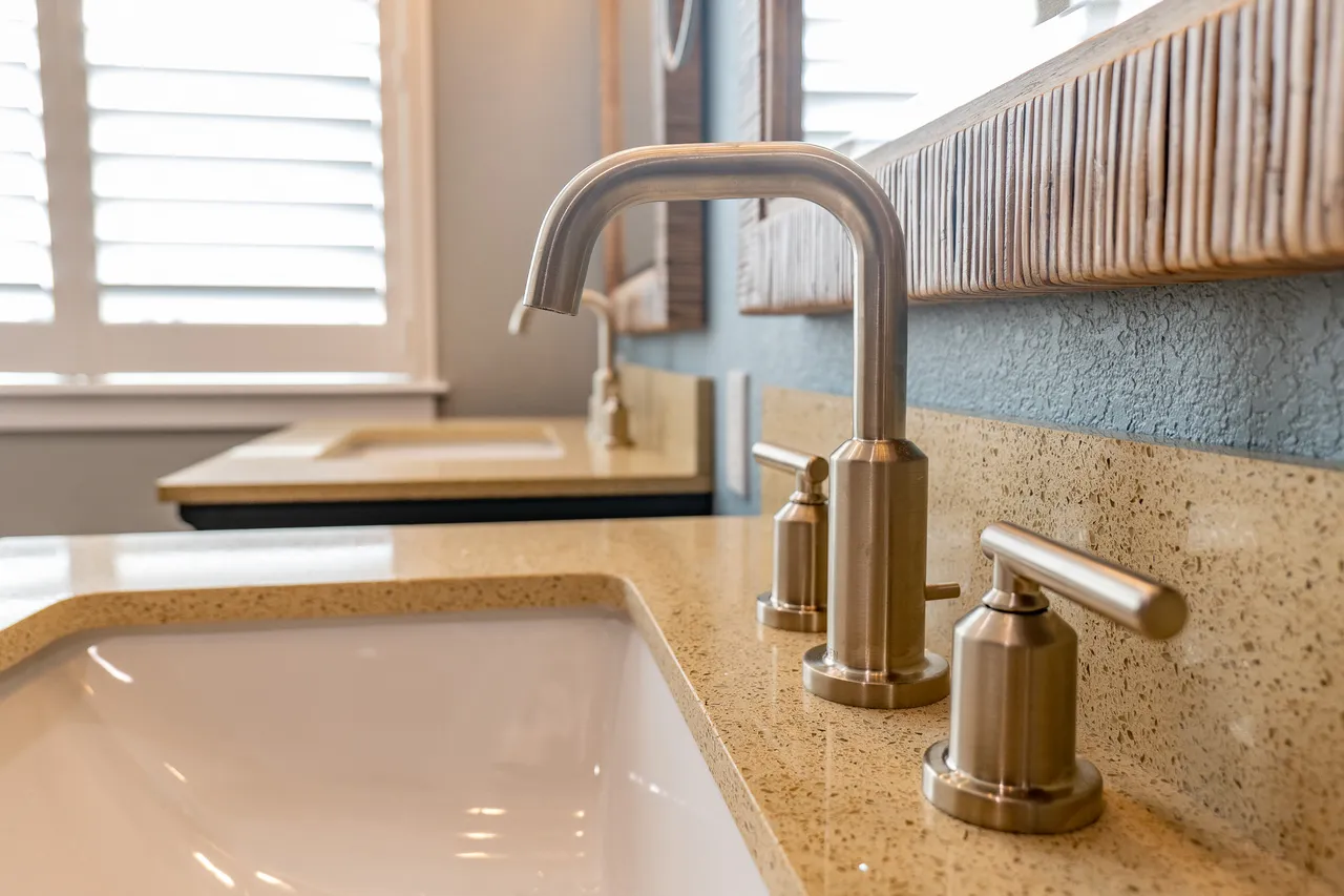 Brushed nickel faucet on a speckled quartz vanity top with a white undermount sink and rattan mirror frame