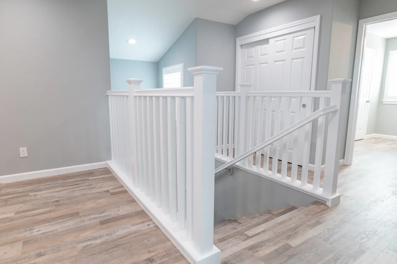 Second-floor landing with white square-newel railing and balusters, gray wood-look floors, and pale blue walls
