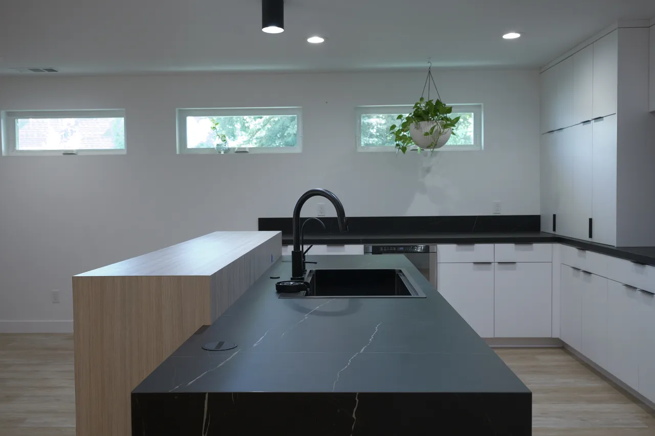 Black stone island with undermount sink beneath three clerestory windows and a hanging plant