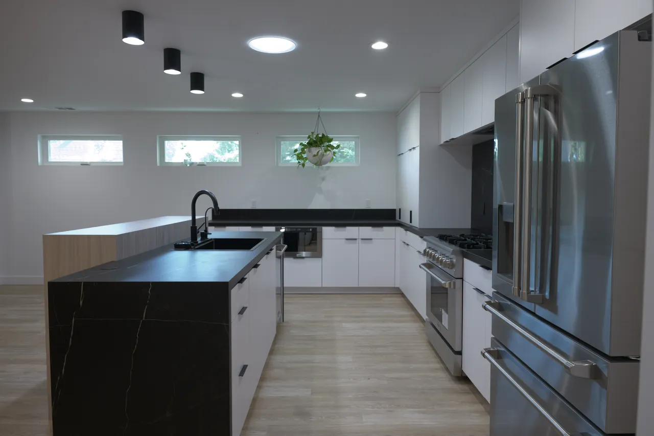 Kitchen with white flat-panel cabinets, black stone backsplash, wood waterfall island, and stainless range and refrigerator