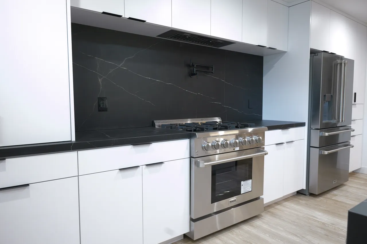 Stainless gas range against a veined black slab backsplash with a matte black pot filler