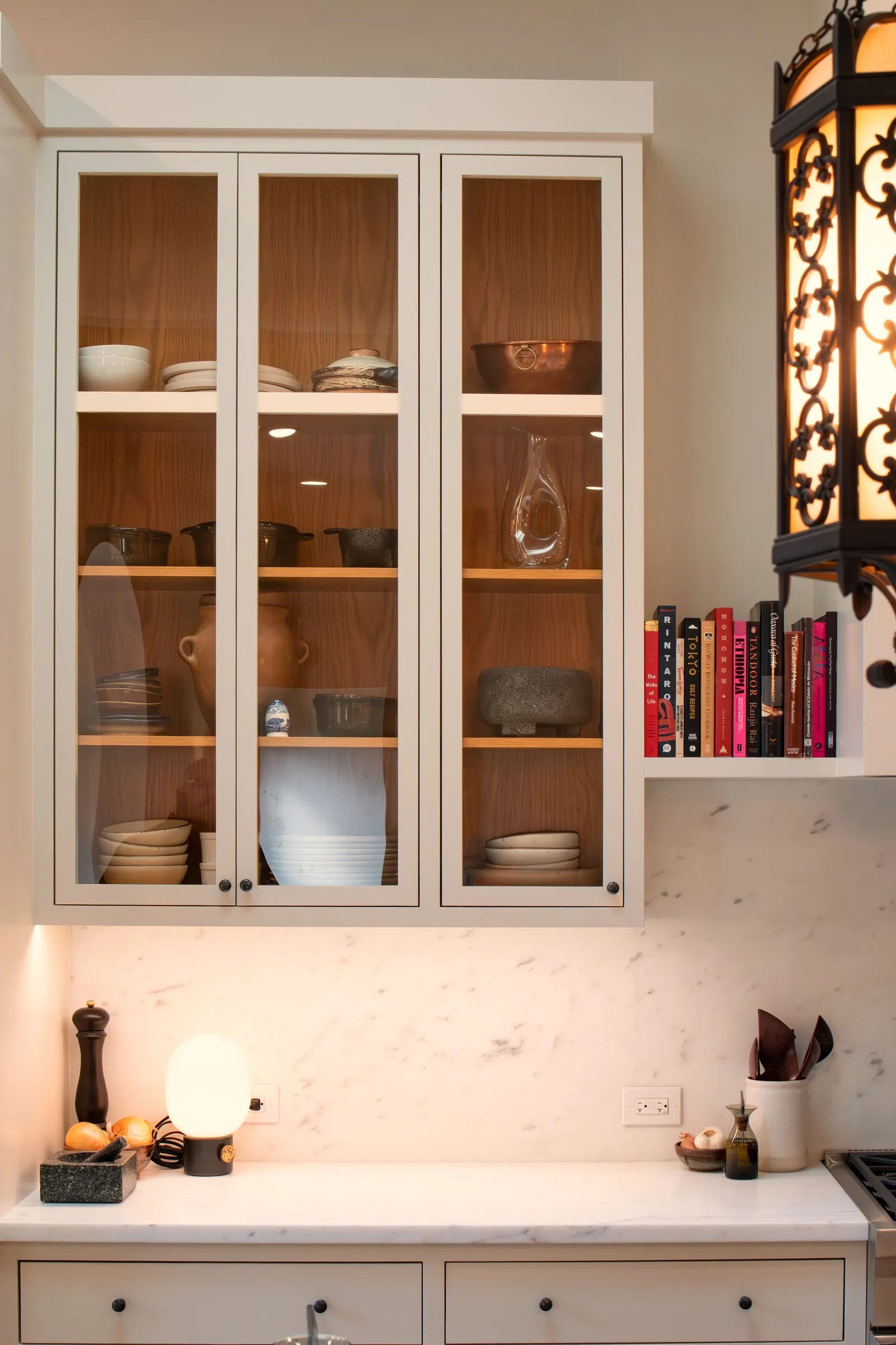 Glass-front upper cabinets lined with plain-sliced white oak, holding ceramics and glassware above a marble counter