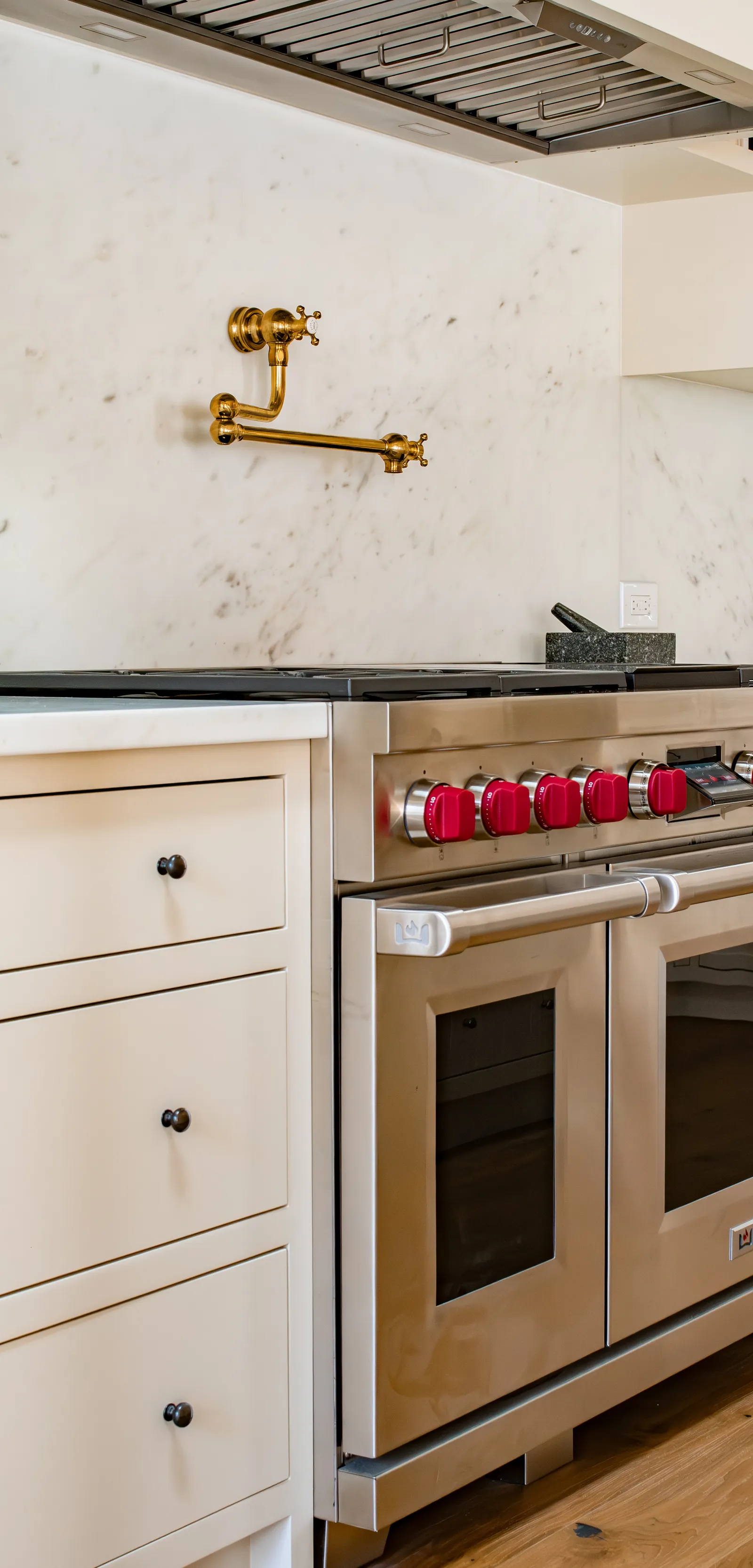 Wolf range with red knobs under a marble slab backsplash with a solid bronze pot filler