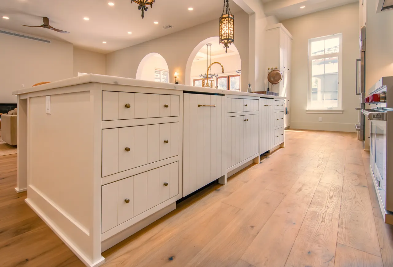 Kitchen island with custom V-groove paneling, wide-plank oak floors, and arched openings beyond